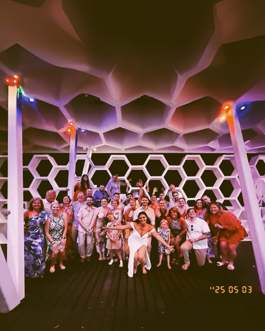 Sara and Tyler gather with a large group beneath a honeycomb-patterned ceiling at their destination wedding.