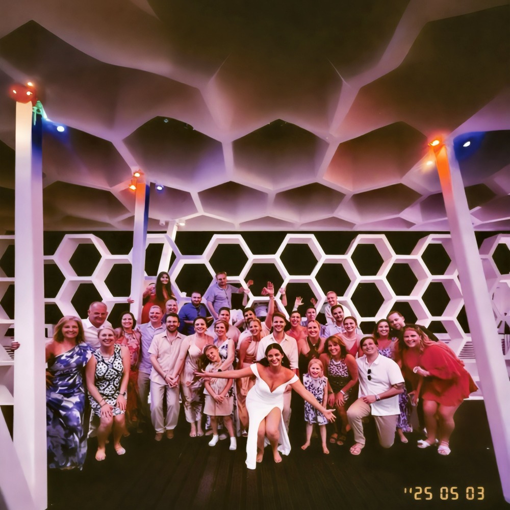 A group of people pose together indoors at a destination wedding, standing in front of a striking honeycomb-patterned wall.
