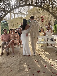 Aubrey and Noah walk down a sandy aisle at their destination wedding, while guests look on from beneath a beautifully decorated canopy.