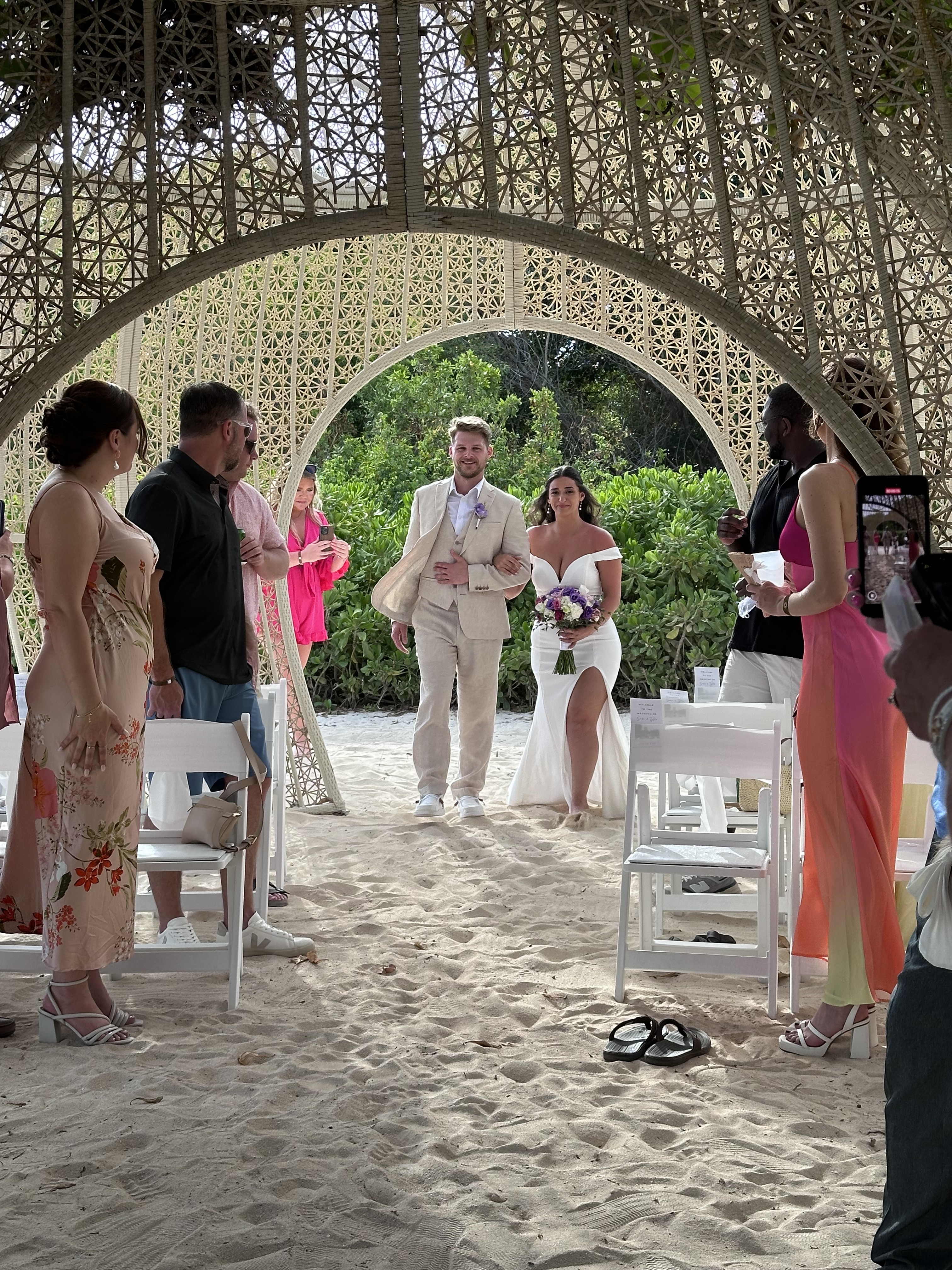 Aubrey and Noah stroll down a sandy aisle at their destination wedding, surrounded by lush greenery and their guests.