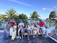A group celebrates a destination wedding with Aubrey and Noah, surrounded by palm trees and ocean views in this picturesque outdoor setting.