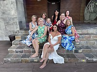 Nine women and a girl in colorful dresses sit on the steps, smiling together at the destination wedding—Aubrey and Noah’s celebration.