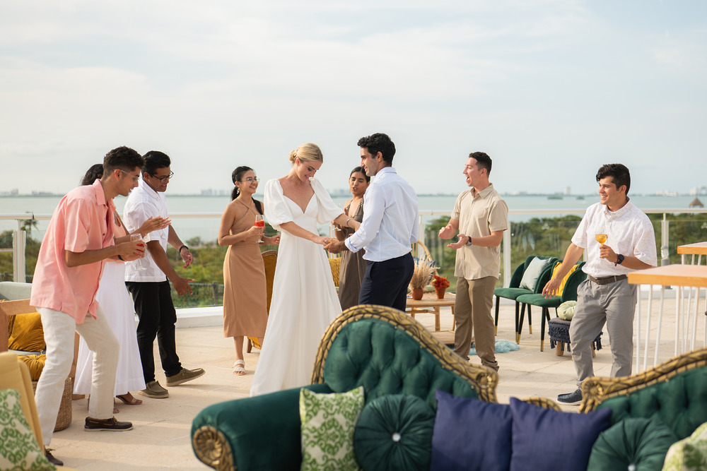 Guests dance and socialize outdoors by green sofas, enjoying the scenic backdrop of a beautiful destination wedding.