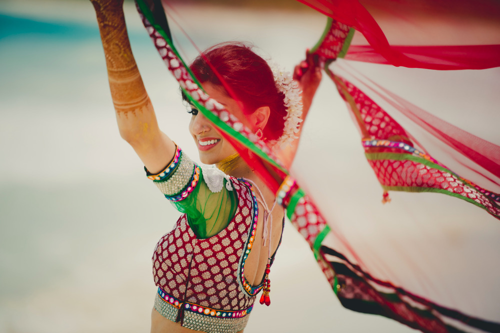 A woman in traditional Indian attire dances gracefully outdoors with a vibrant dupatta, celebrating at a colorful destination wedding.