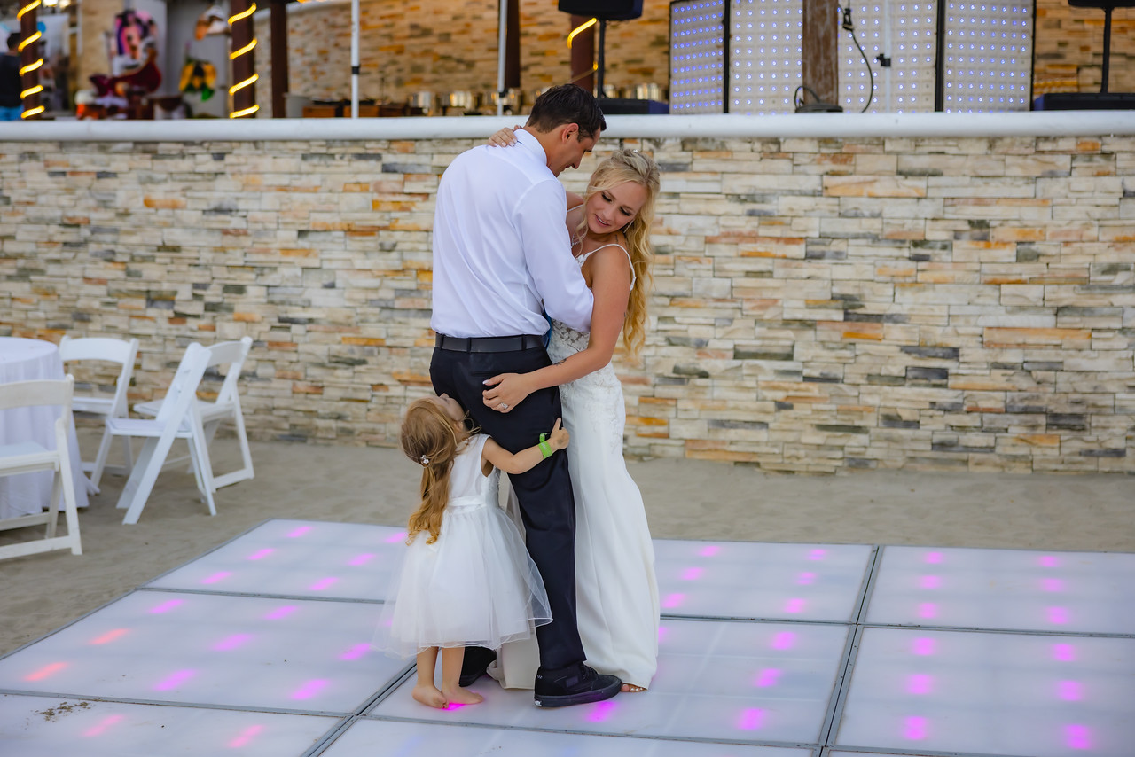 Camille and Jeff share a joyful dance with a young girl in white dresses on the illuminated floor at their destination wedding.