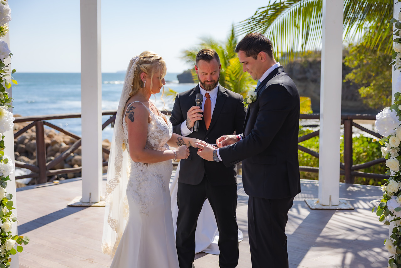 During their destination wedding by the ocean, Camille and Jeff exchange rings in a beautiful outdoor ceremony.