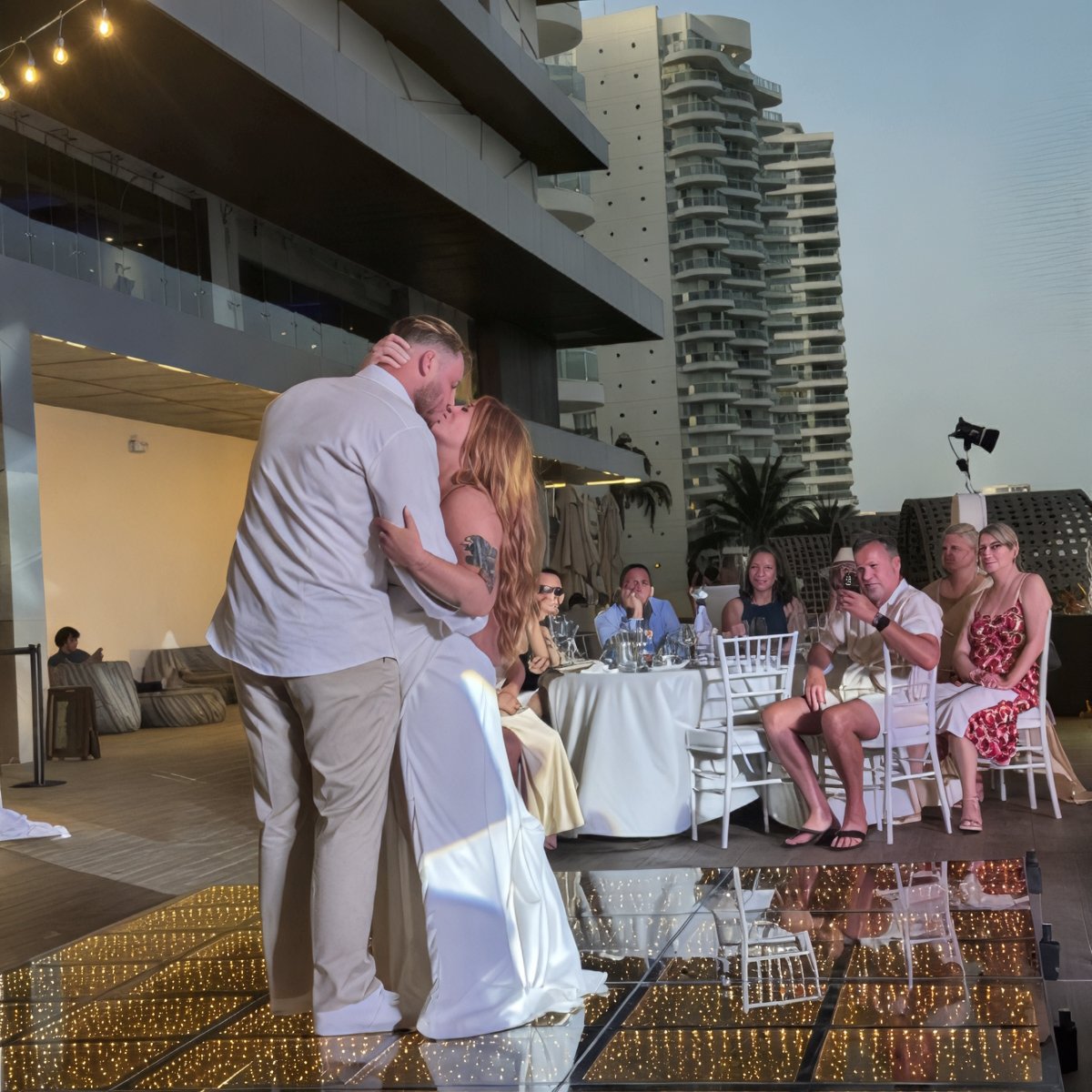 At their destination wedding, Alexis and Colton share a kiss on a reflective dance floor while guests look on from outside.
