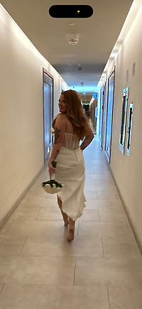 A woman, barefoot and smiling, walks down the hallway with flowers in hand, wearing the Alexis and Colton dress—radiating joy on her destination wedding day.