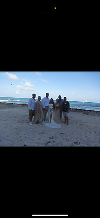 Alexis and Colton: Six people pose together on a sandy beach with the ocean in the background, capturing a beautiful moment from their destination wedding.