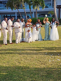 Cynthia and Ruben's destination wedding party poses outdoors, dressed elegantly in white and light blue attire.