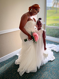 At a destination wedding, a bride in white poses with a young girl dressed in white, holding a basket.