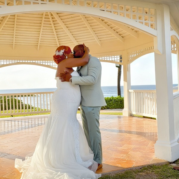 Cynthia and Ruben share a kiss beneath a white gazebo overlooking the ocean on their destination wedding day.