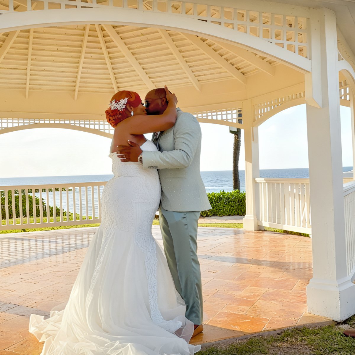 Cynthia and Ruben share a kiss beneath a white gazebo overlooking the ocean on their destination wedding day.
