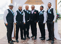 Six men dressed in Natoya and Katrina vests and dress shirts stand at a beachside wedding altar, ready for the destination wedding ceremony.