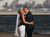 Natoya and Katrina embrace and smile on the beach beneath a cloudy sky during their destination wedding.