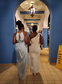 Natoya and Katrina walk arm-in-arm through a blue, archway-lined corridor at night, savoring a magical moment during their destination wedding.