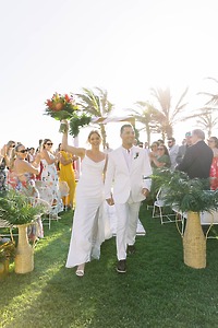 Alexis and Colton walk down the aisle at their destination wedding, cheered on by guests and surrounded by swaying palm trees.