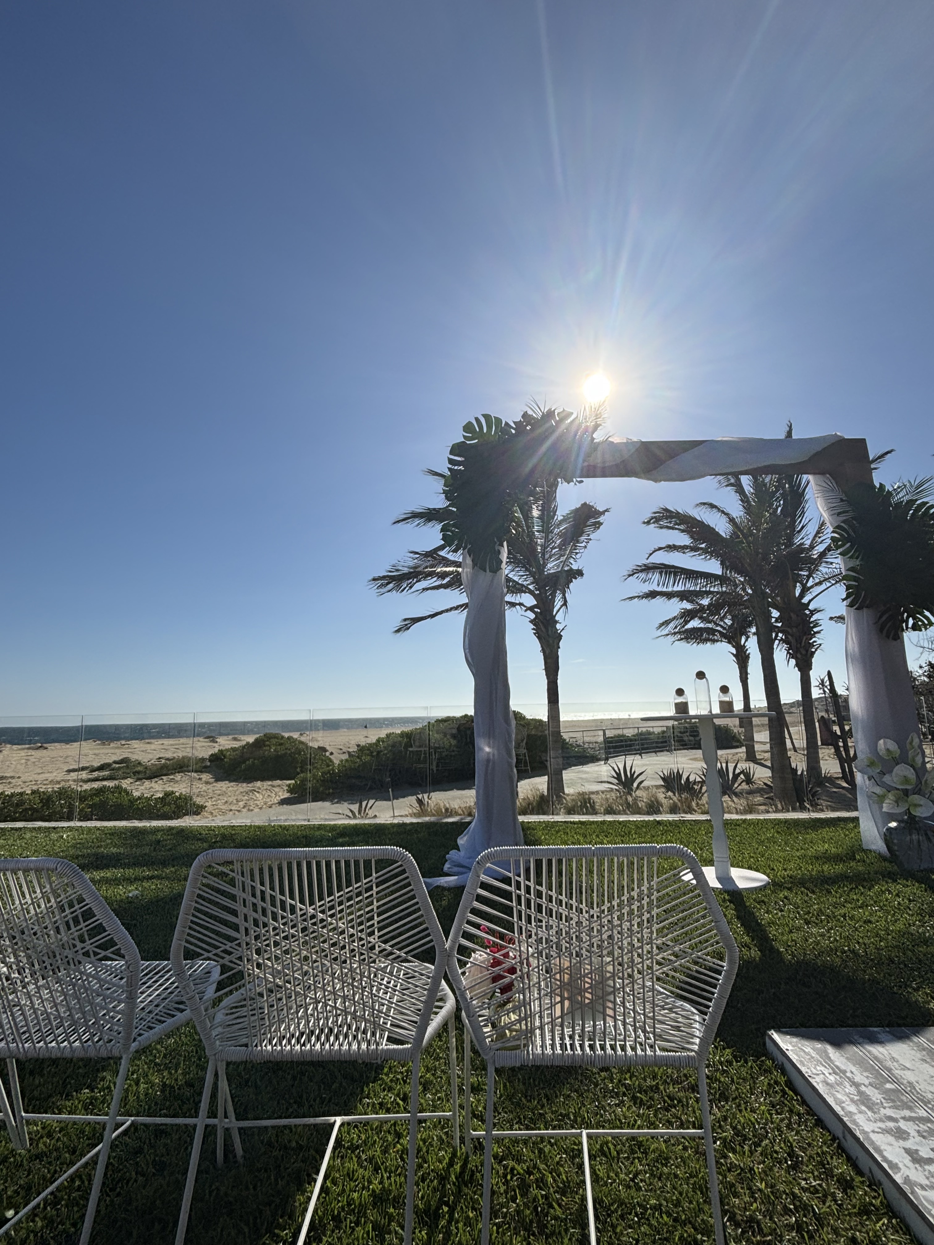 Rows of white chairs are arranged on the beach, facing a wedding arch for Alexis and Colton’s destination wedding under a clear blue sky.