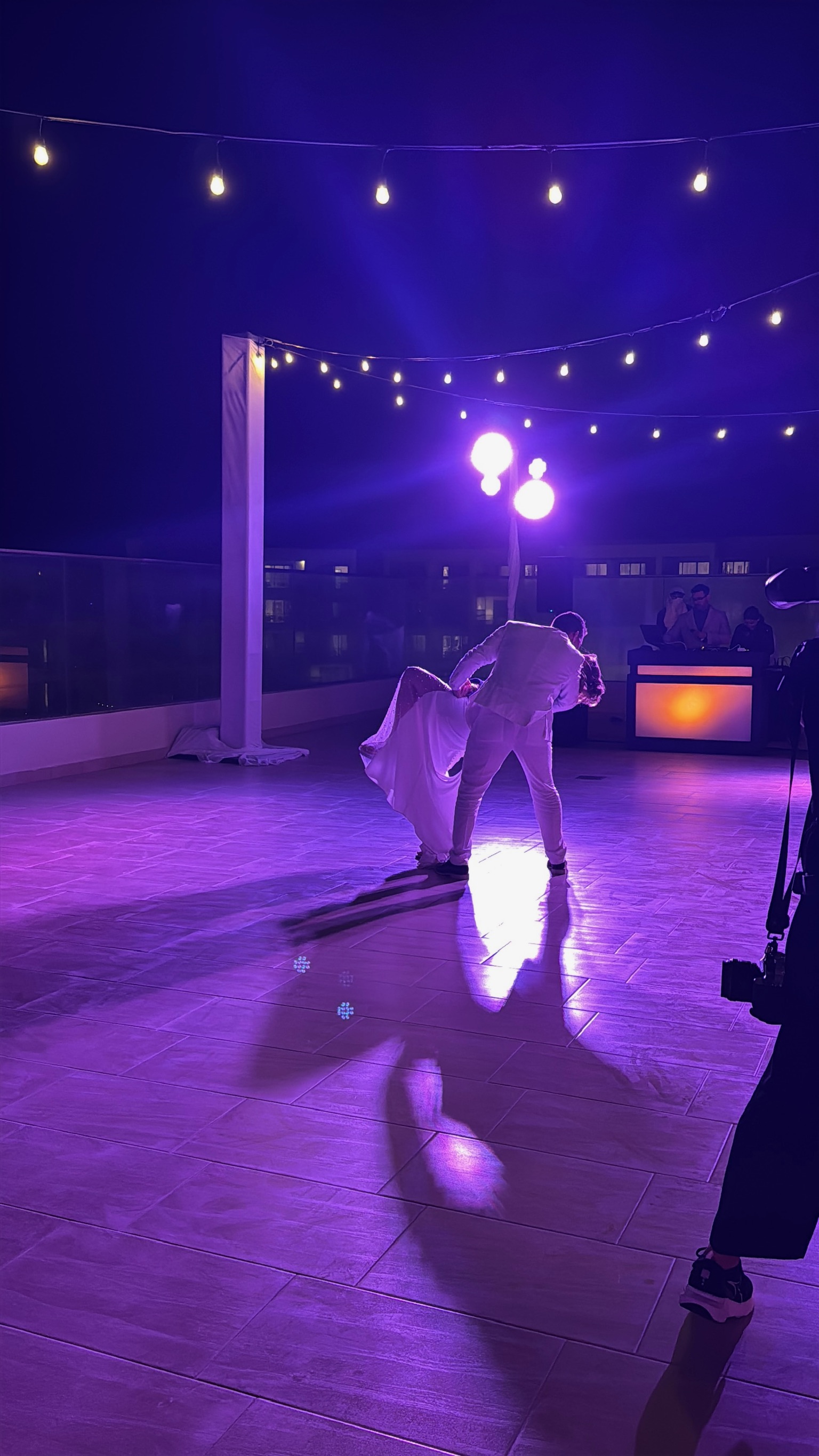 Alexis and Colton share a romantic dance on a rooftop at night beneath purple lights during their destination wedding.