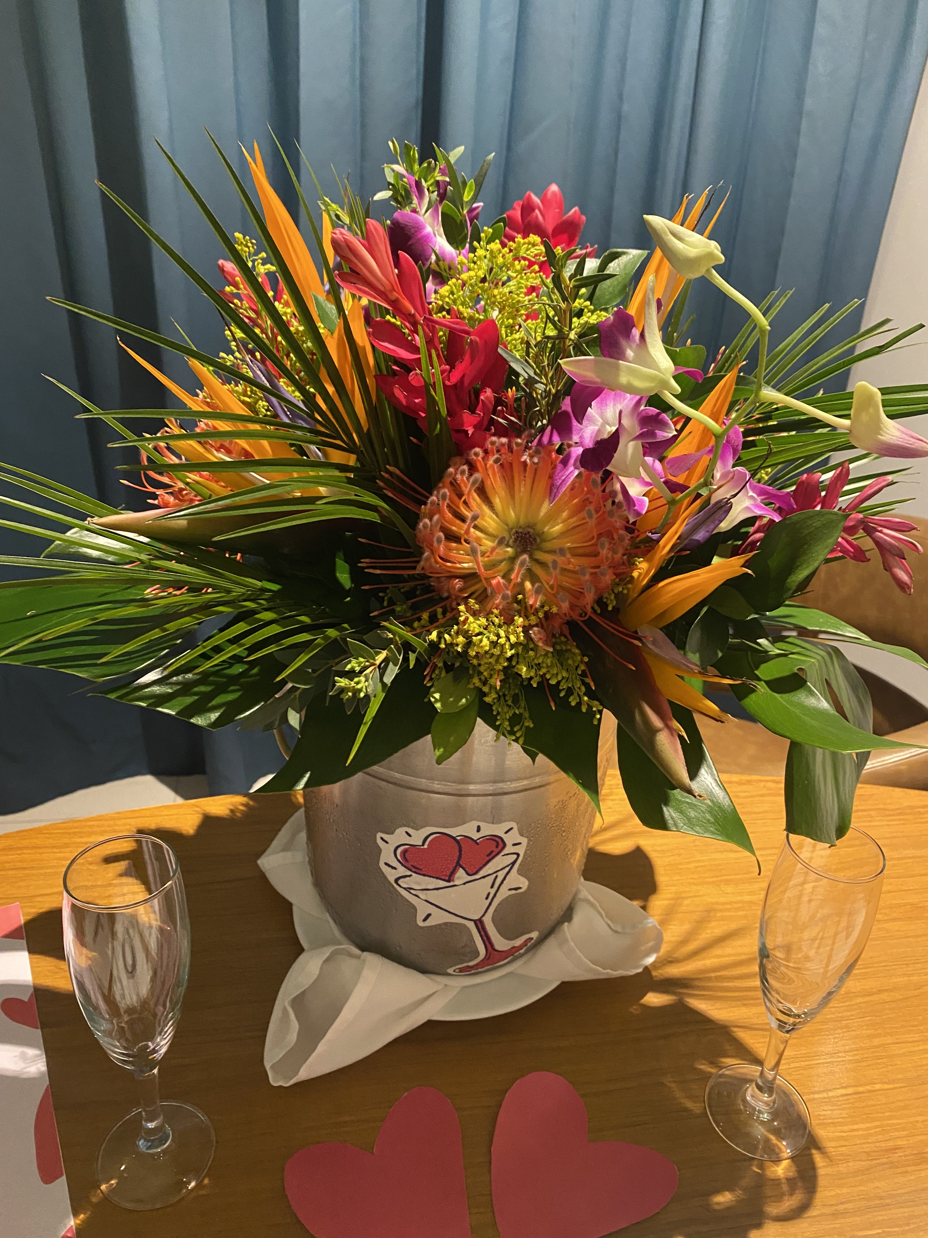 A beautiful wedding bouquet in a vase sits on the table alongside champagne glasses and decorative paper hearts—perfect for a romantic destination wedding celebration.