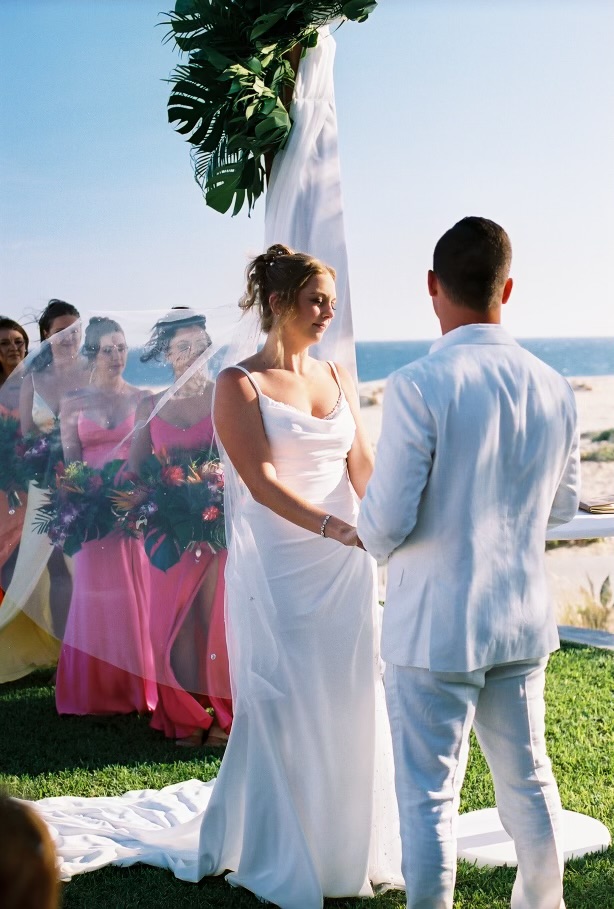 Alexis and Colton stand facing each other during their destination wedding ceremony on the beach.