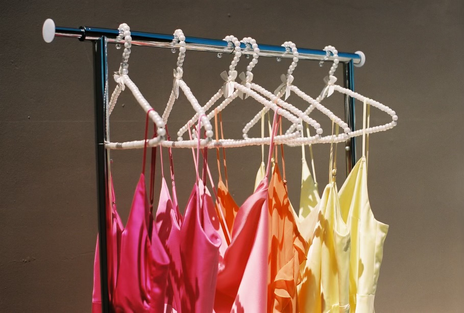 Alexis and Colton (Copy) wedding guest dresses in pink, orange, and yellow hang on a rack with white hangers—perfect choices for a destination wedding celebration.