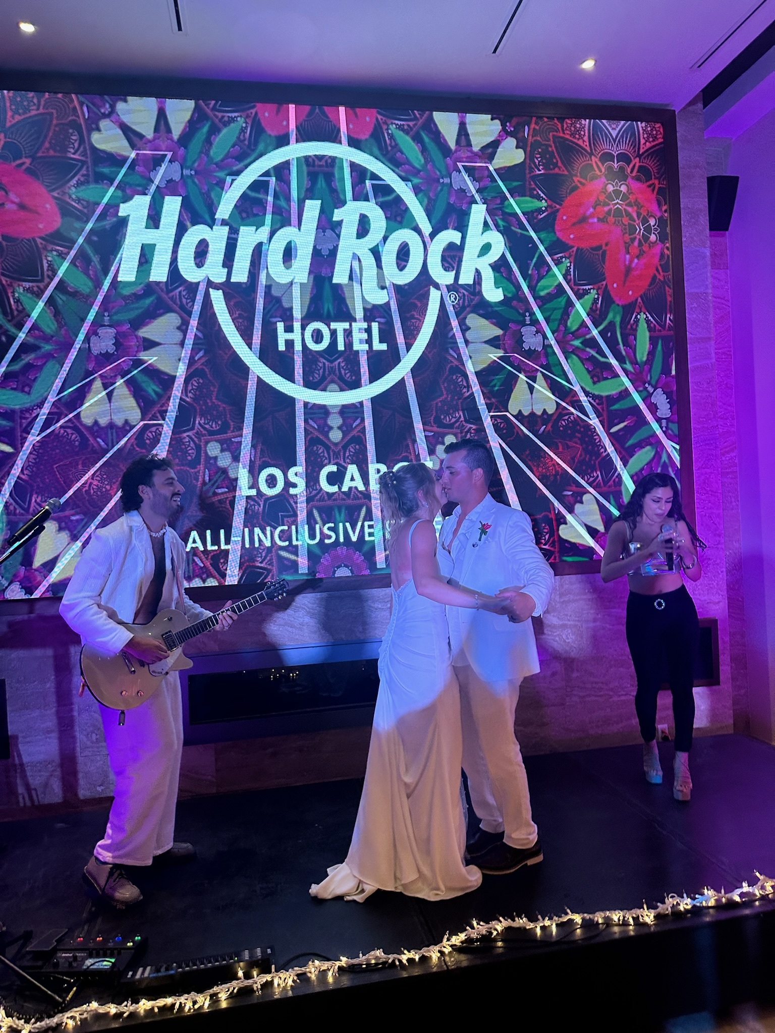 Alexis and Colton share a dance on stage at the Hard Rock Hotel during their destination wedding, while a live band plays in the background.