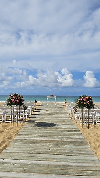 Tiana and Steven's destination wedding features a beautiful beachside aisle lined with white chairs and elegant flower arrangements.