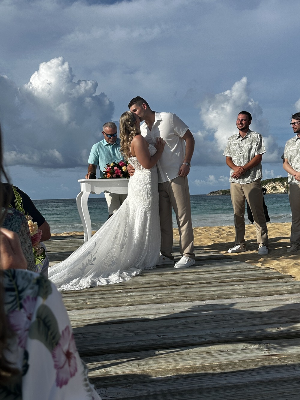 Tiana and Steven share a kiss at their destination wedding on the beach, surrounded by their officiant and guests looking on.