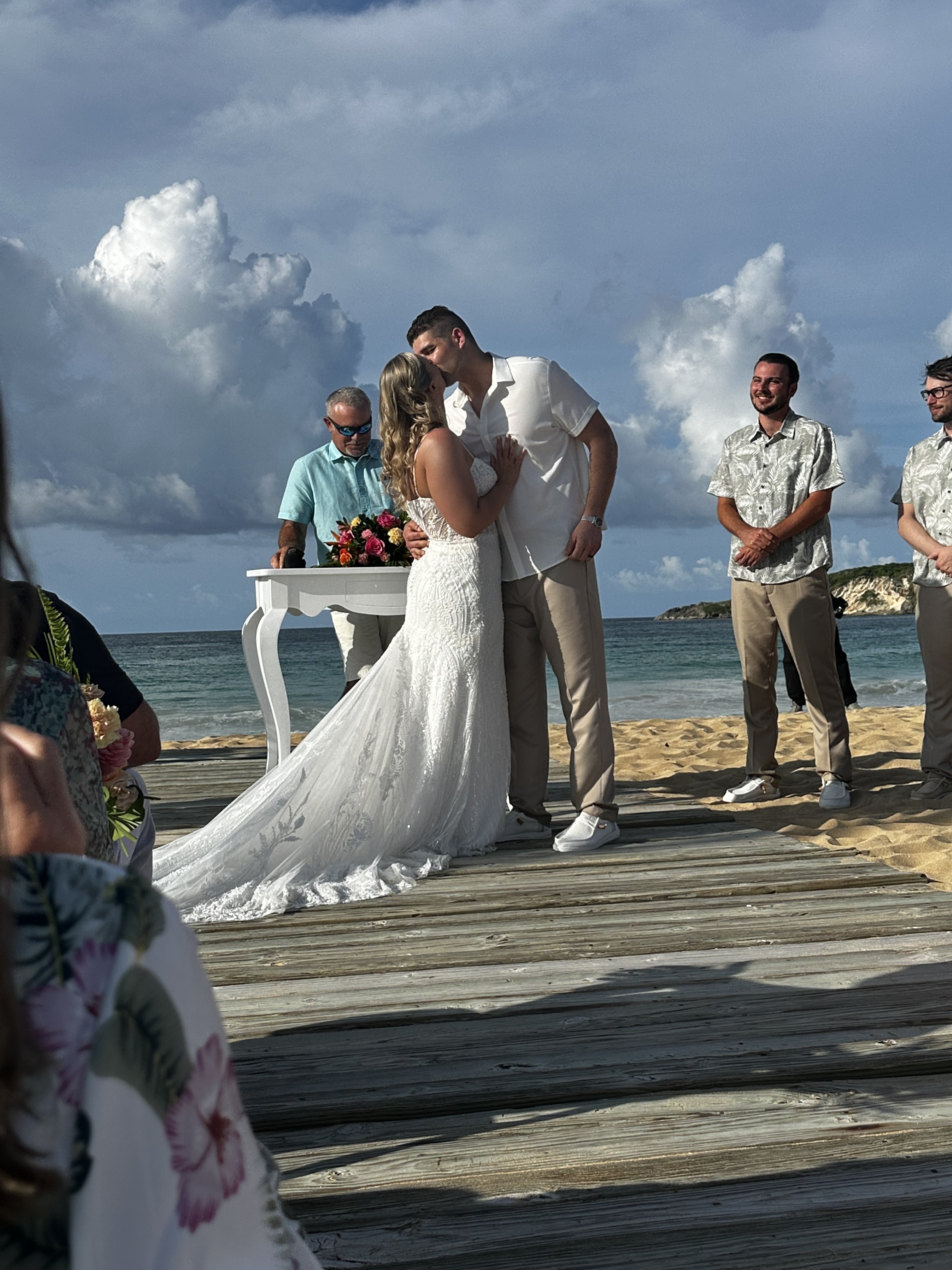 Tiana and Steven share a kiss at their destination wedding on the beach, surrounded by their officiant and guests looking on.