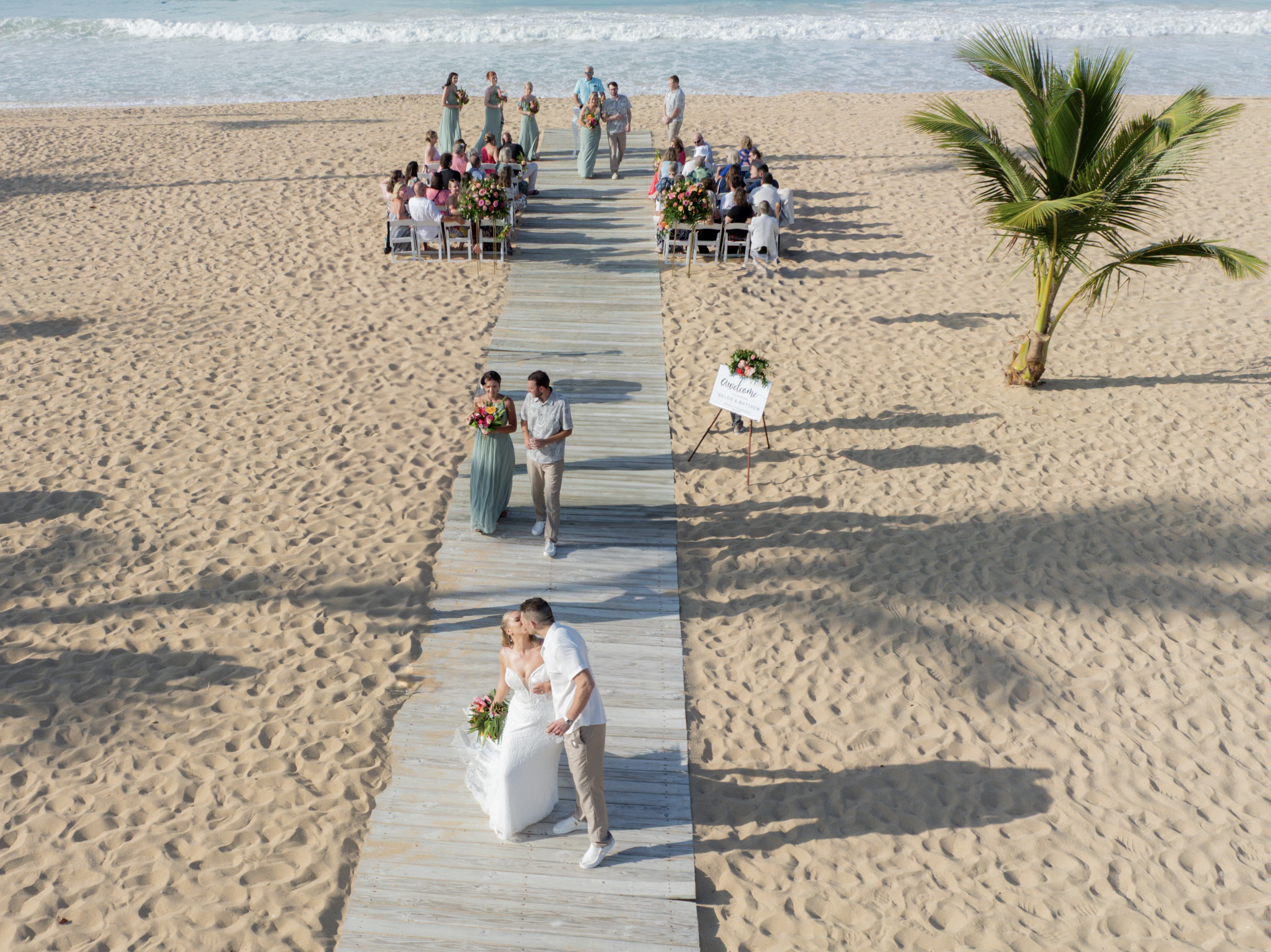Tiana and Steven share a romantic kiss on a wooden walkway during their beautiful destination wedding by the beach.