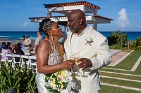 Khadijah and Oscar share a joyful smile outdoors, dressed in wedding attire and holding wine glasses and a bouquet, capturing a beautiful moment from their destination wedding.