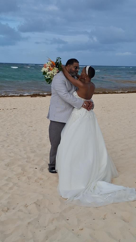 Jamie and Gary share an embrace on the sandy beach, the ocean serving as a breathtaking backdrop to their destination wedding.