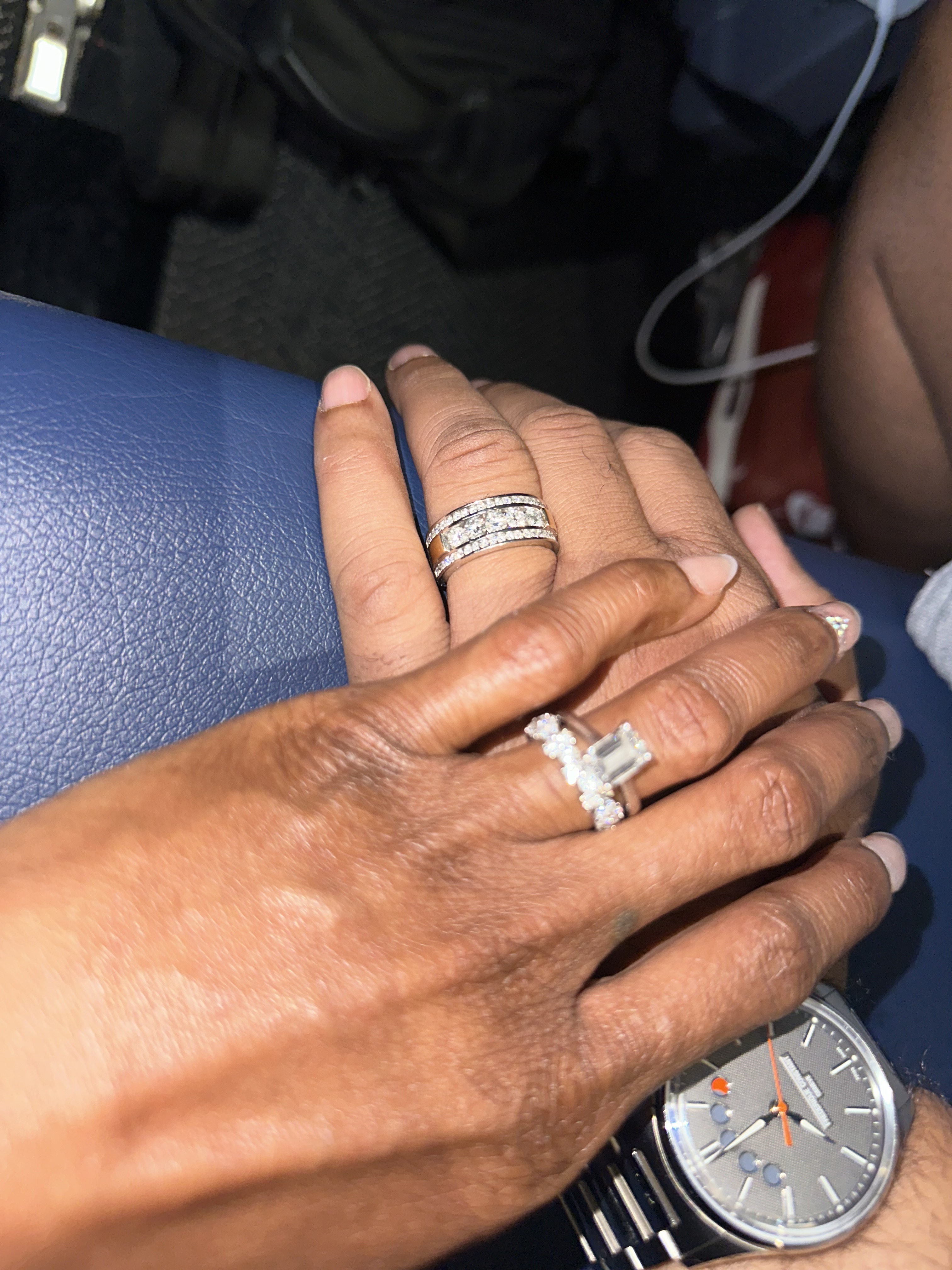 Jamie and Gary hold hands on a blue surface, their wedding rings prominently displayed; one of them also wears a silver watch—capturing a special moment from their destination wedding.