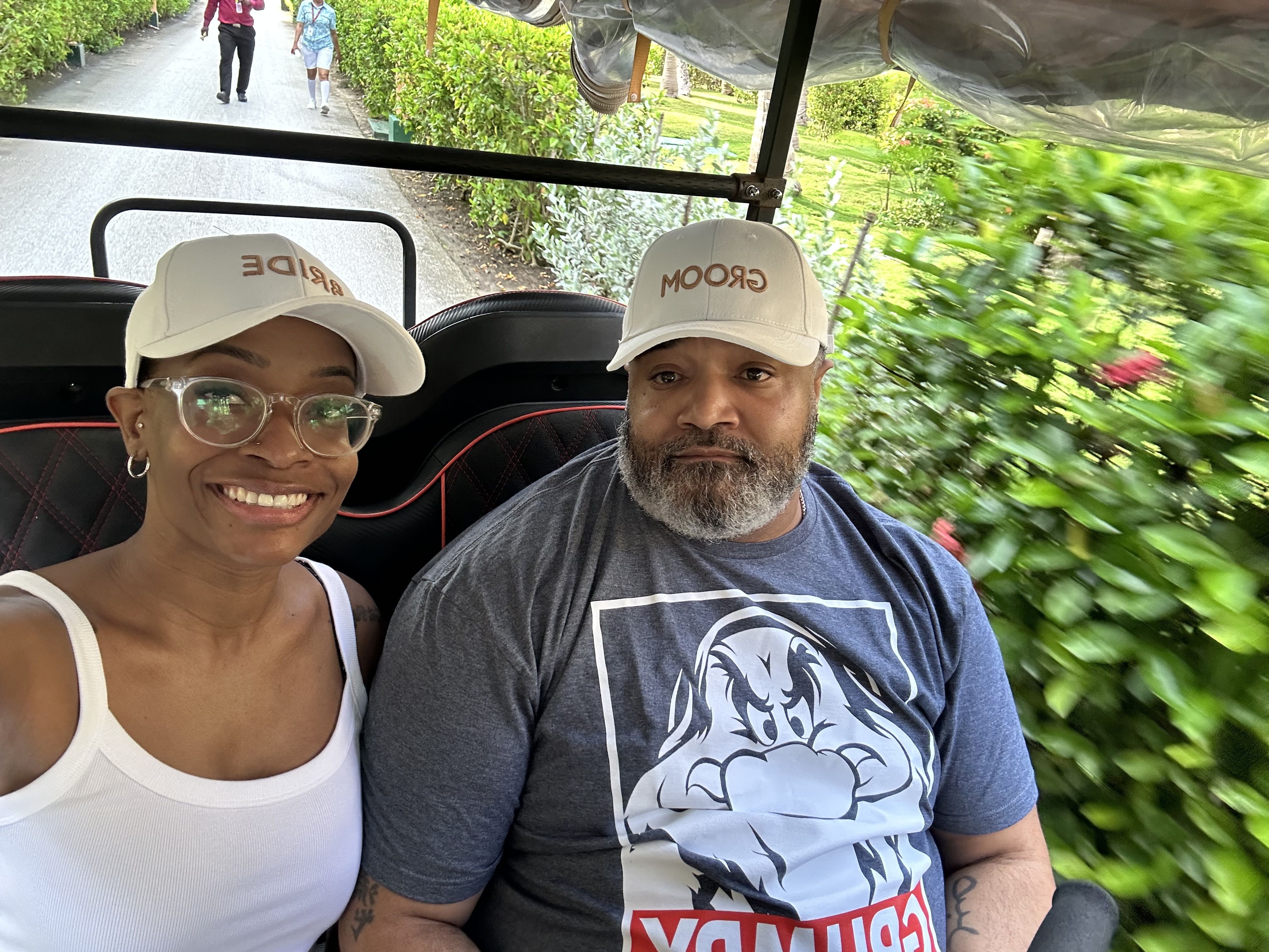 Jamie and Gary, both sporting matching hats, enjoy a ride together through lush greenery on their destination wedding day.