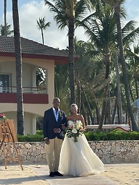 Jamie and Gary stroll outside near swaying palm trees and a luxurious villa, savoring the atmosphere of their destination wedding.