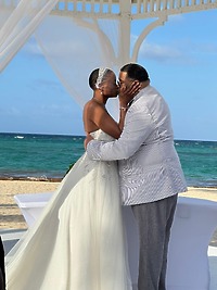 Jamie and Gary share a kiss beneath a white gazebo during their beautiful outdoor beach destination wedding ceremony.