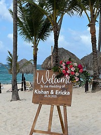 Wooden wedding welcome sign for Jamie and Gary’s destination wedding, set on a sandy beach with palm trees.