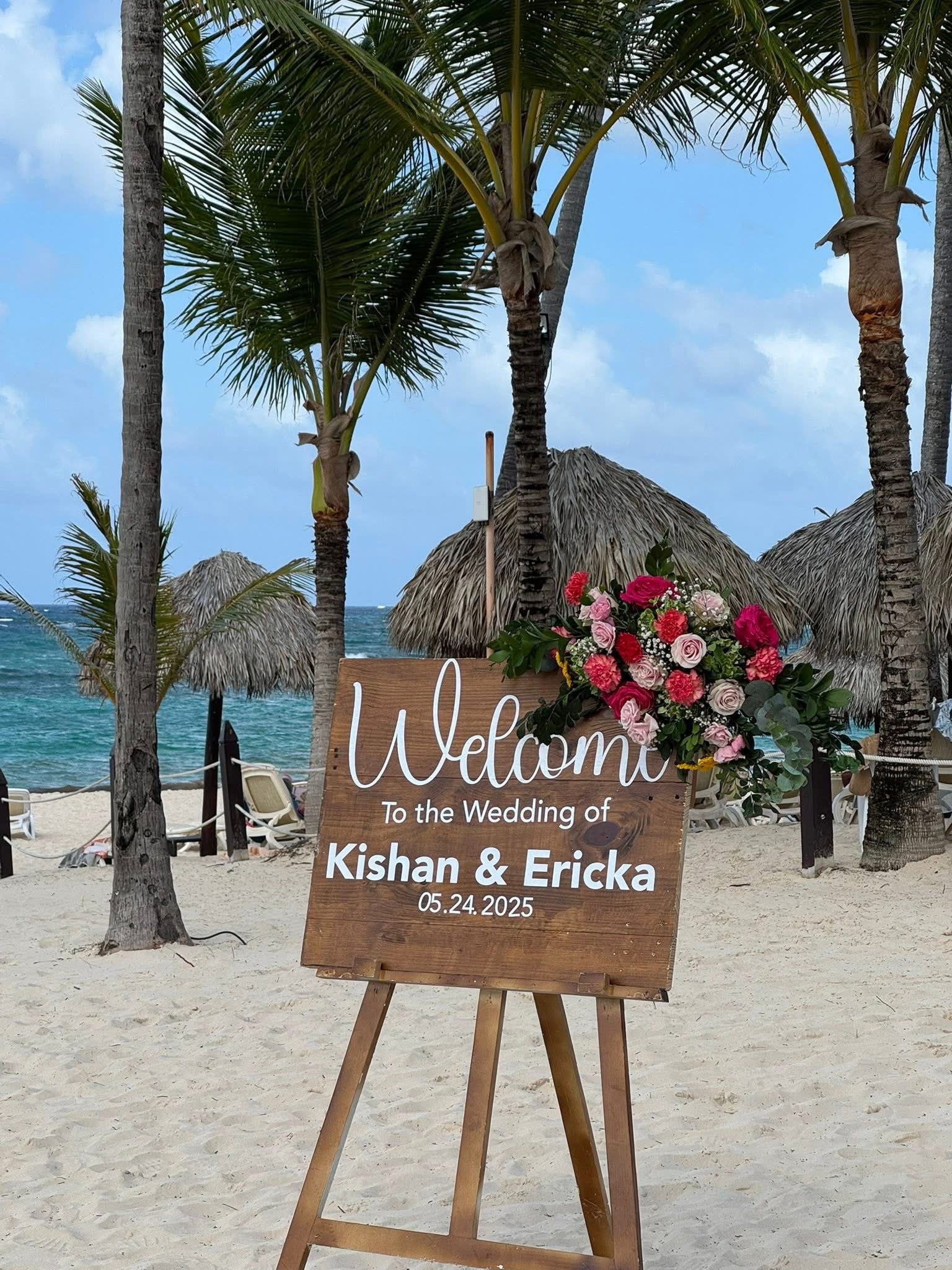 Wooden wedding welcome sign for Jamie and Gary’s destination wedding, set on a sandy beach with palm trees.