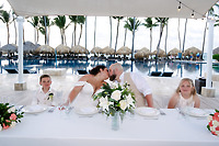 Kelsie and Matthew share a kiss at their destination wedding, seated at a poolside table with their two children by their side.