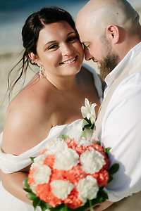 Kelsie and Matthew embrace outdoors during their destination wedding, holding a bouquet of white and coral flowers.