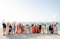 Kelsie and Matthew (Copy): A wedding party dressed in formalwear gathers on a beach, raising their arms and smiling as they celebrate a joyful destination wedding.
