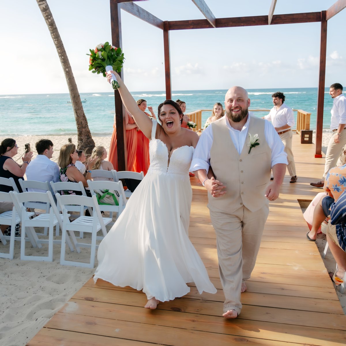 Kelsie and Matthew walk down the aisle on the sandy beach as wedding guests look on, celebrating the bride at their beautiful destination wedding.