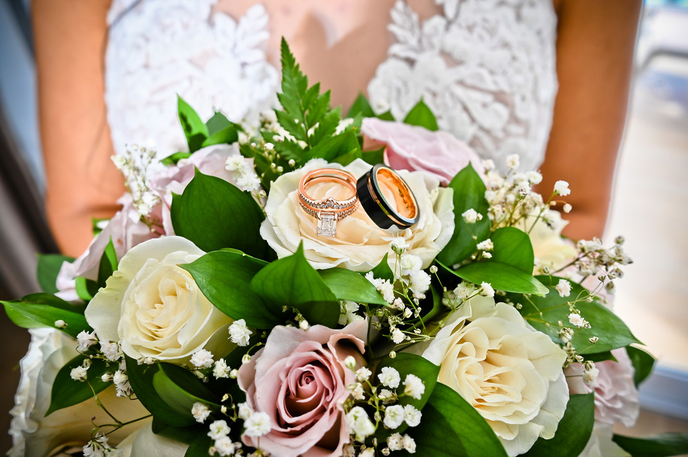 Bridal bouquet for a destination wedding, featuring white and pink roses, lush greenery, and two wedding rings resting on top.