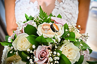 Bridal bouquet for a destination wedding, featuring white and pink roses, lush greenery, and two wedding rings resting on top.