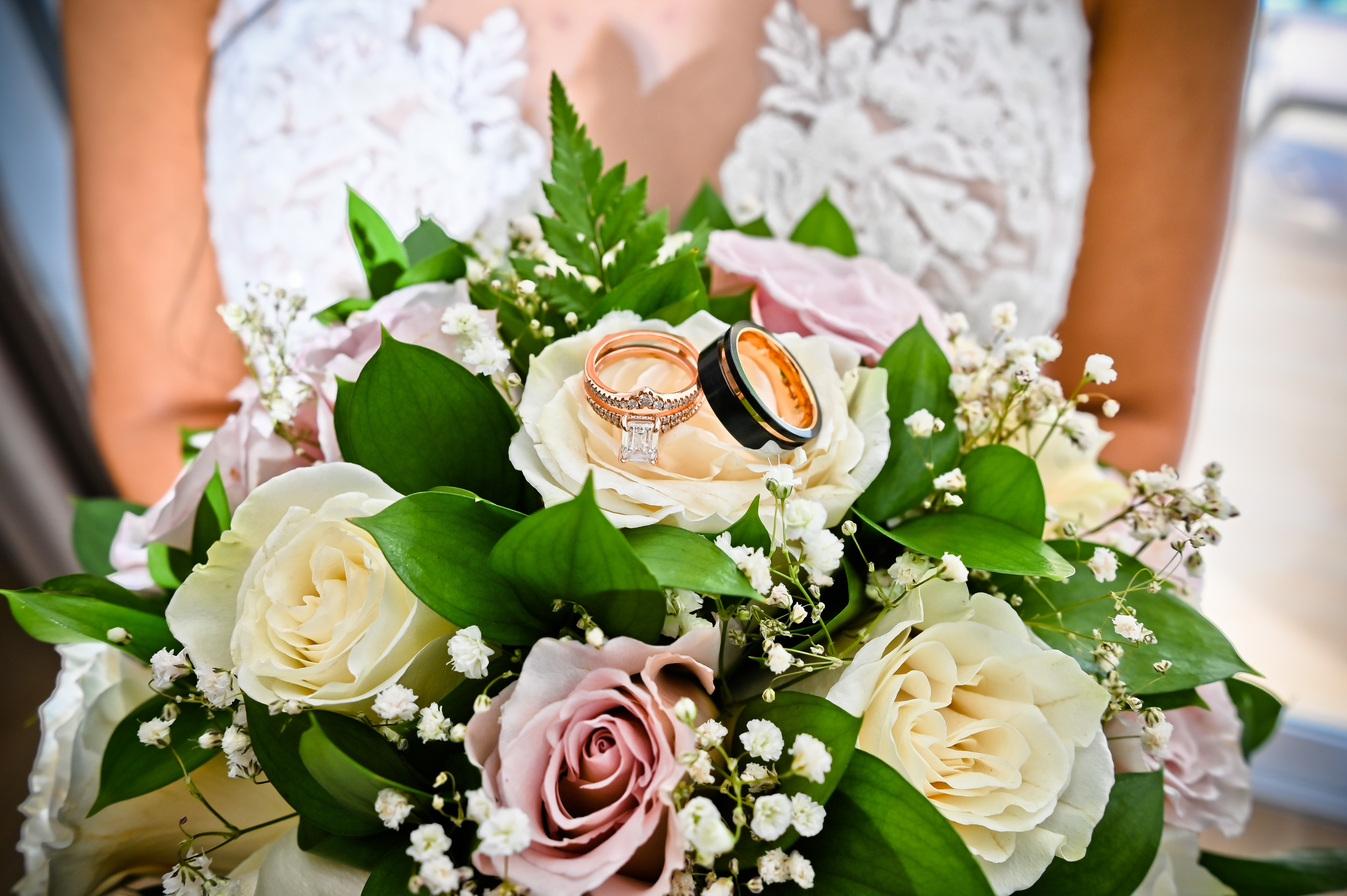 Bridal bouquet for a destination wedding, featuring white and pink roses, lush greenery, and two wedding rings resting on top.