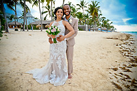 Trey and Kimberly pose together on a sandy beach lined with palm trees, capturing a beautiful moment from their destination wedding.