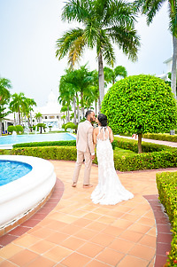 Trey and Kimberly stroll along a tiled pathway by the pool, surrounded by palm trees and lush gardens at their destination wedding.