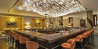 Moon Palace Nizuc: a modern hotel bar ideal for destination weddings, featuring elegant marble counters, vibrant orange chairs, and striking hanging glassware.