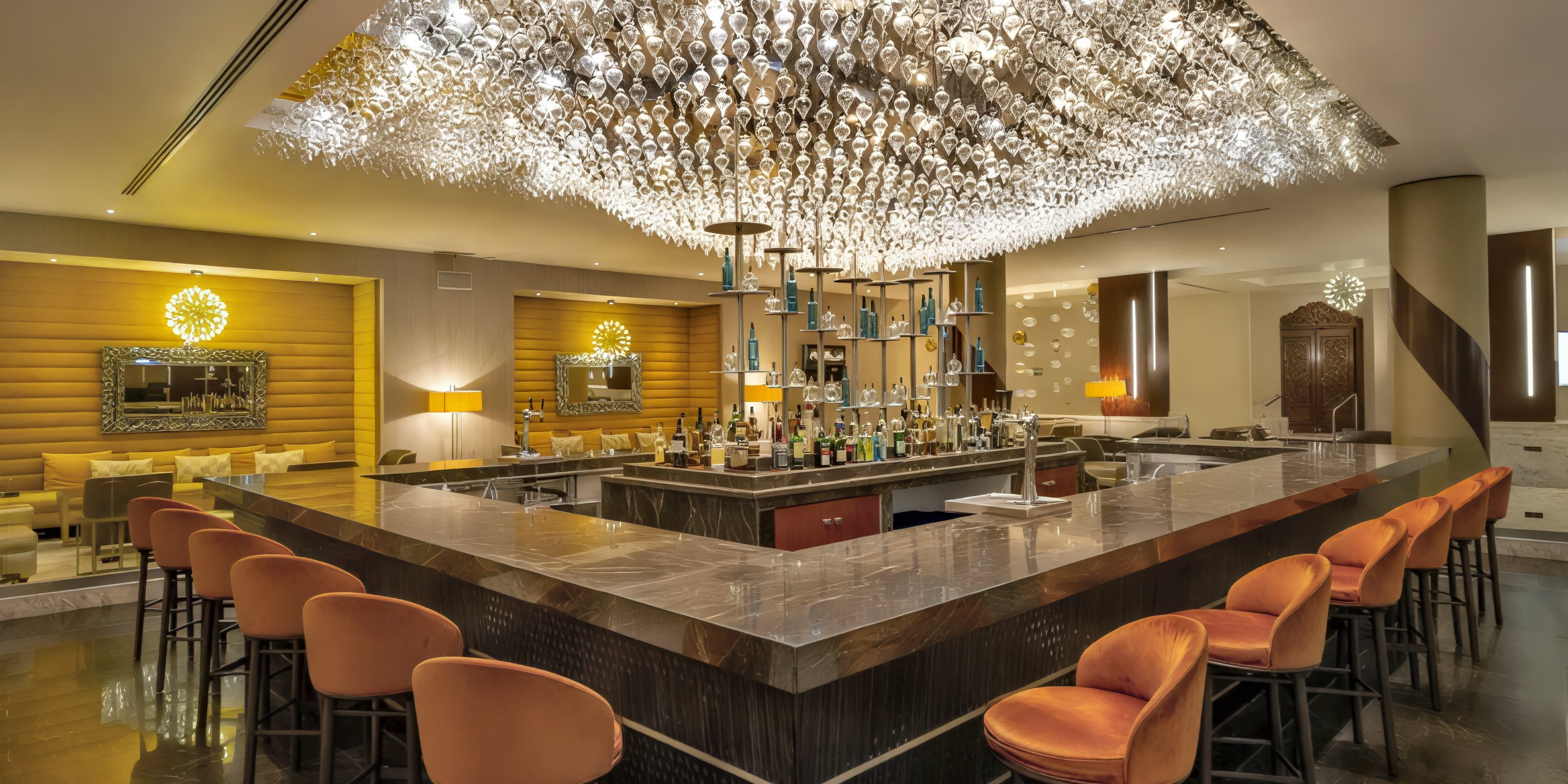 Moon Palace Nizuc: a modern hotel bar ideal for destination weddings, featuring elegant marble counters, vibrant orange chairs, and striking hanging glassware.